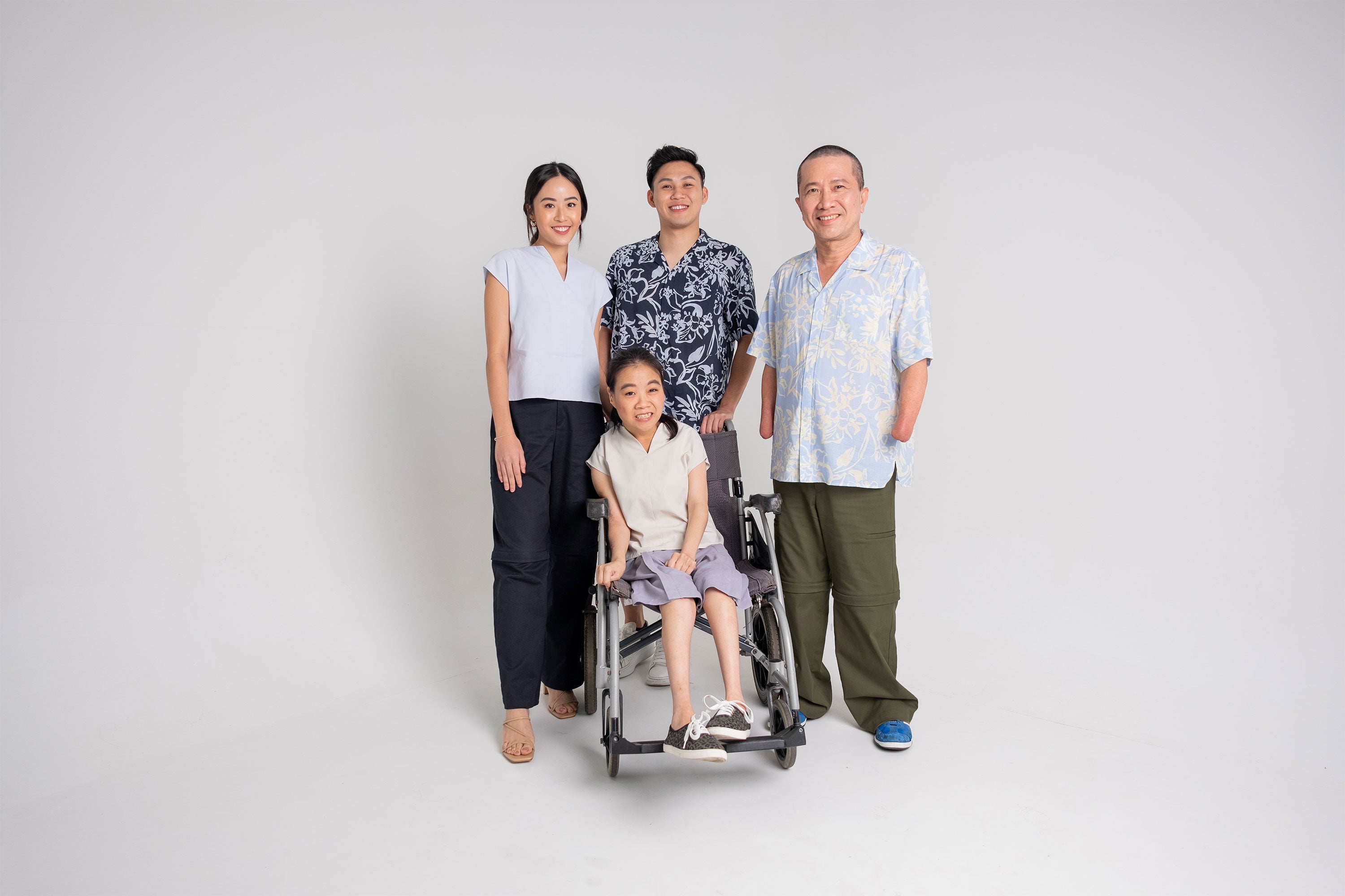 A group photo of four; a young able-bodied woman, a young able-bodied man, a middle-aged man with amputated arms, and a middle-aged woman seated on a wheelchair.